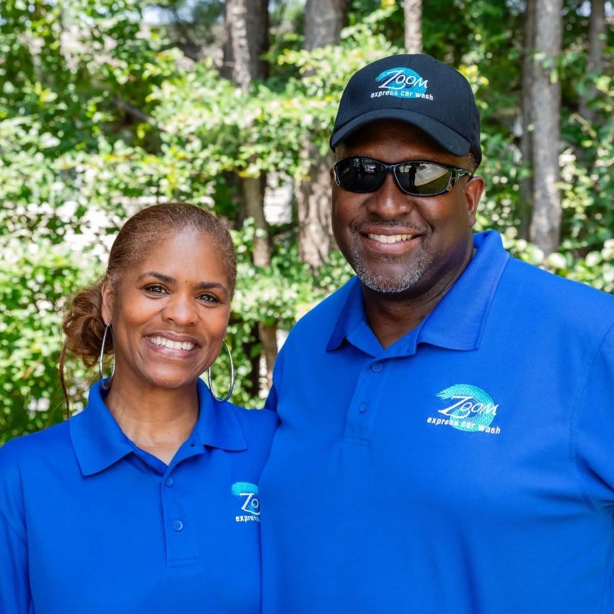 Two smiling Zoom Express team members in branded blue polos, one in a Zoom cap