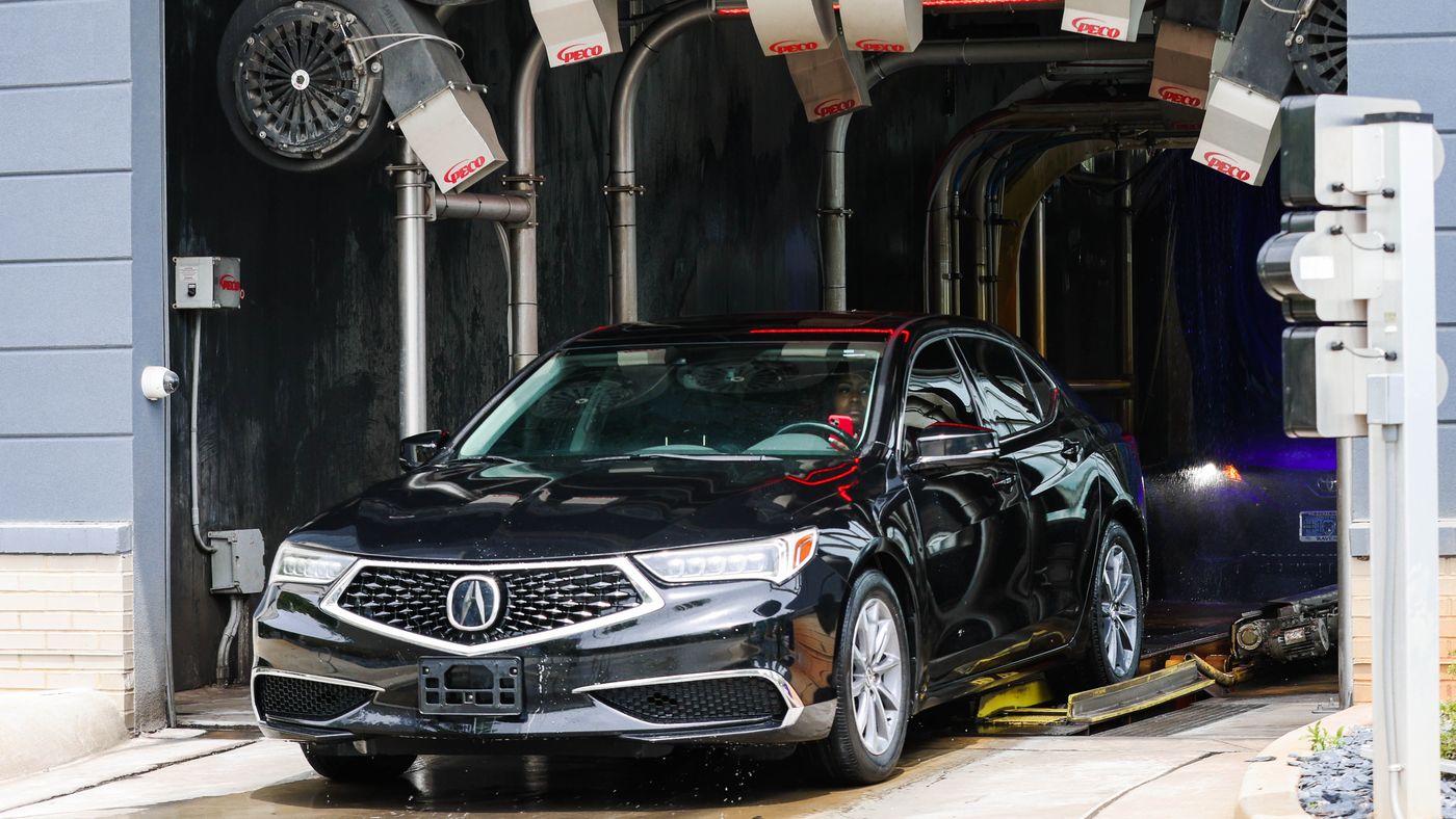 A freshly washed black sedan rolling out of the Zoom Express tunnel under the dryers